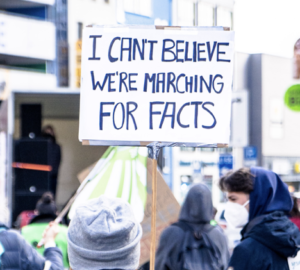 Manifestantes em protesto ambiental com cartaz sobre desinformação climática