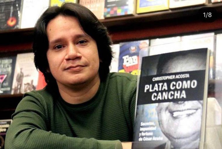 Jornalista peruano Christopher Acosta, de camisa de mangas compridas na cor verde sentado ao lado de seu livro. Ao fundo, vários outros livros. Ele tem cabelos escuros em comprimento médio.