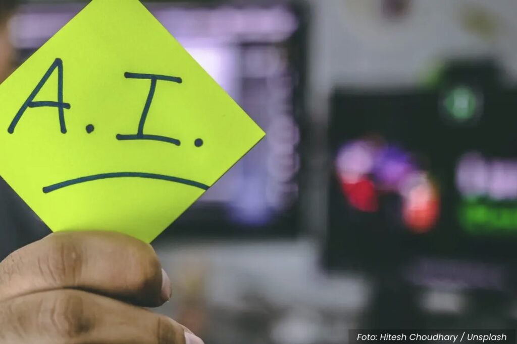 Homem segura post it com letras IA em um ambiente de trabalho como uma redação jornalística