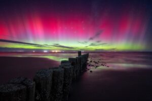 A foto mostra o horizonte iluminado pelos navios ancorados e a aurora boreal no céu