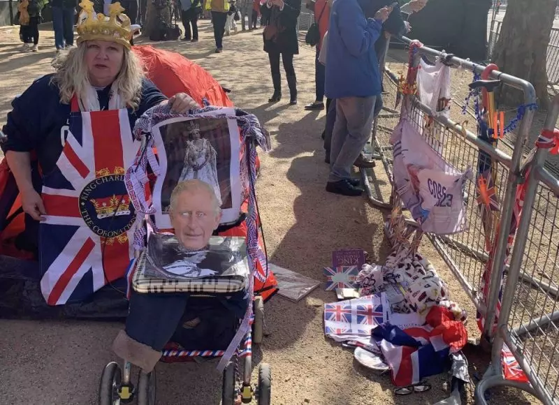 Mulher com coroa e símbolos em homenagem ao rei Charles e à rainha Elizabeth esperando a passagem do cortejo da coroação em Londres