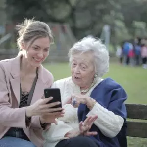mulher jovem e idosa usando celular na praça.