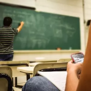 Professor escreve no quadro enquanto aluna olha o smartphone, que na opinião da Unesco deve ser proibido nas escolas