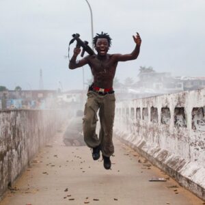 Comandante da milícia liberiana segurando arma comemora em uma ponte na Libéria. A foto foi selecionada pela Getty Images para o Dia Mundial da Fotografia