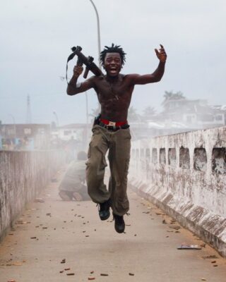 Comandante da milícia liberiana segurando arma comemora em uma ponte na Libéria. A foto foi selecionada pela Getty Images para o Dia Mundial da Fotografia