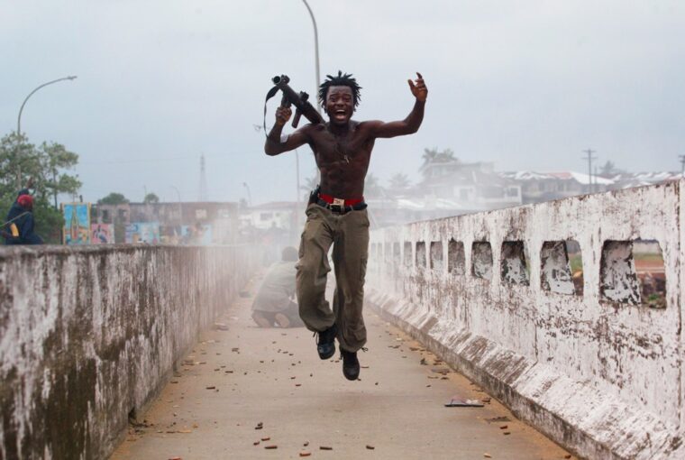 Comandante da milícia liberiana segurando arma comemora em uma ponte na Libéria. A foto foi selecionada pela Getty Images para o Dia Mundial da Fotografia