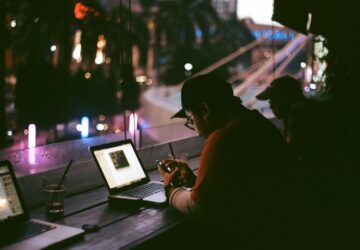 Homem em café com smartphone e notebook acessando a internet, que tem a liberdade ameaçada em vários países