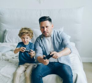 Pai e filho jogam videogame sentados na cama; estudo aponta que jogos podem ajudar a diminuir o estresse em curto prazo