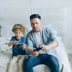 Pai e filho jogam videogame sentados na cama; estudo aponta que jogos podem ajudar a diminuir o estresse em curto prazo