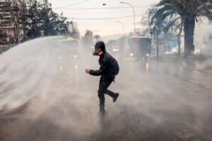 Manifestante fugindo após atirar uma garrafa contra a polícia durante a comemoração dos 50 anos do Golpe Militar no Chile