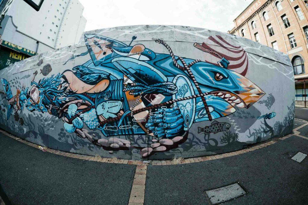Arte de rua retratando tubarão e peixes em situação de risco