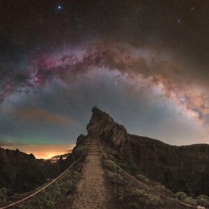 Via Láctea fotografada em arco sobre colina rochosa na Ilha da Madeira, Portugal, com nebulosas vermelhas visíveis.
