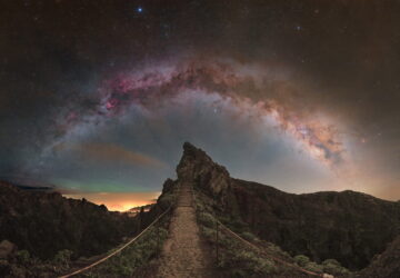 Via Láctea fotografada em arco sobre colina rochosa na Ilha da Madeira, Portugal, com nebulosas vermelhas visíveis.
