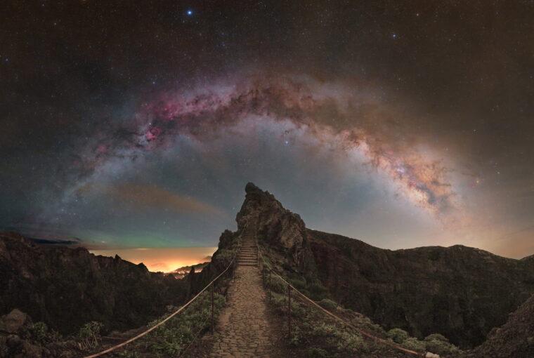 Via Láctea fotografada em arco sobre colina rochosa na Ilha da Madeira, Portugal, com nebulosas vermelhas visíveis.