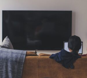 Jovem com TV desligada lendo no computador, refletindo mudança de hábitos de consumo de mídia