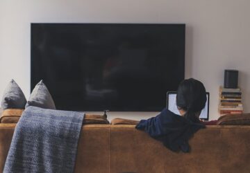 Jovem com TV desligada lendo no computador, refletindo mudança de hábitos de consumo de mídia