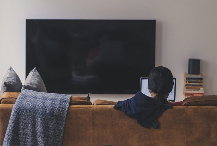 Jovem com TV desligada lendo no computador, refletindo mudança de hábitos de consumo de mídia