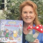 Sarah Ferguson em jardim mostrando um de seus livros infantis