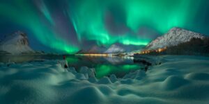 Aurora boreal entre montanhas e um lago na Noruega. A imagem foi premiada no Epson Pano Awards