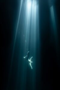 Um homem submerso na água iluminado por um feixe de luz . A imagem foi premiada no concurso de fotos coloridas