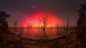 A aurora boreal em tons de vermelho refletida em um lago no Canadá