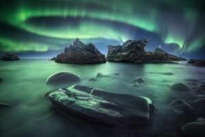 Uma praia de pedras e rochas e as luzes da aurora na Península Rybachy, na Rússia