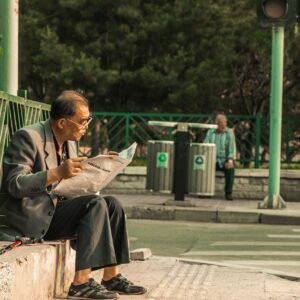 Homem lendo jornal em parque com latas de reciclagem ao fundo