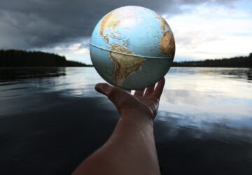 Mão segurando globo terrestre com rio ao fundo