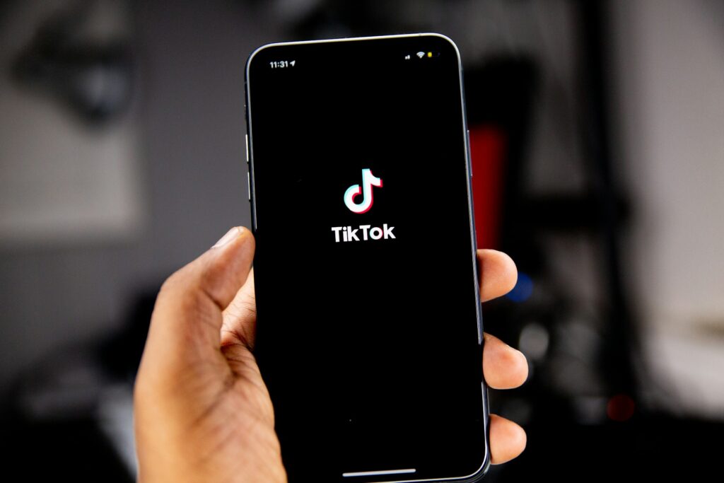 Mão segurando smartphone com tela de acesso ao TikTok