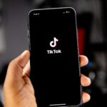 Mão segurando smartphone com tela de acesso ao TikTok