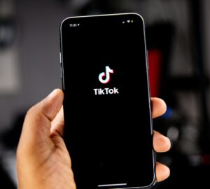 Mão segurando smartphone com tela de acesso ao TikTok