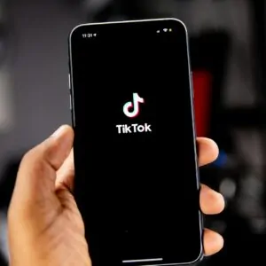 Mão segurando smartphone com tela de acesso ao TikTok