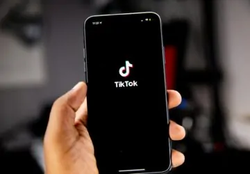 Mão segurando smartphone com tela de acesso ao TikTok