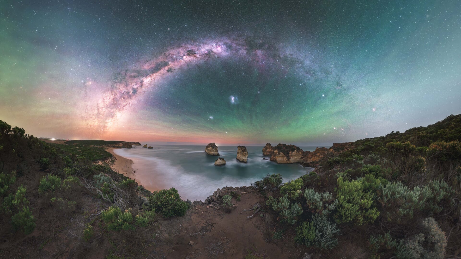 Céu esverdeado com aurora e a Via Láctea sobre Diamond Beach, Austrália.