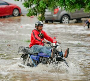 Homem em moto atravessando área alagada na República Dominicana, efeito da crise climática na América Latina