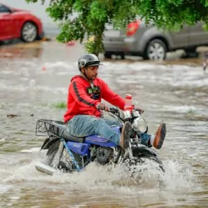 Homem em moto atravessando área alagada na República Dominicana, efeito da crise climática na América Latina