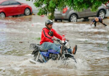 Homem em moto atravessando área alagada na República Dominicana, efeito da crise climática na América Latina