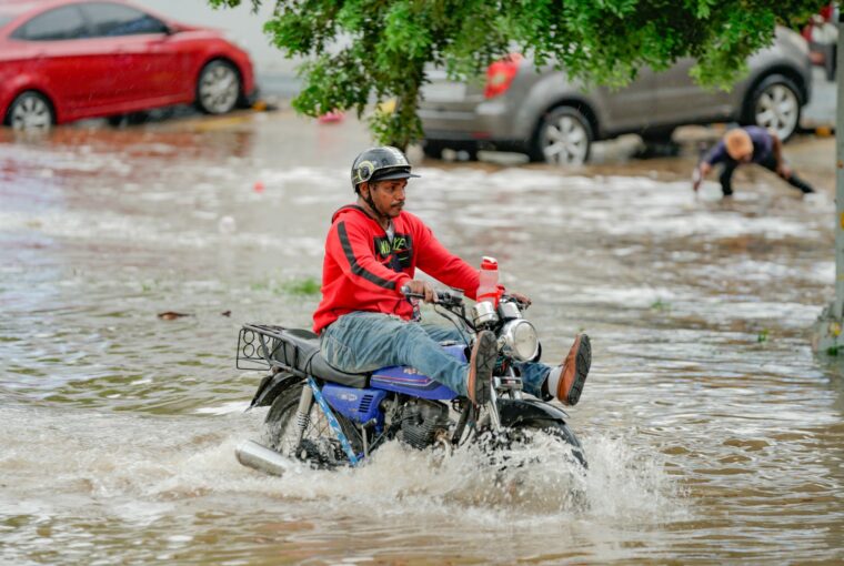 Homem em moto atravessando área alagada na República Dominicana, efeito da crise climática na América Latina
