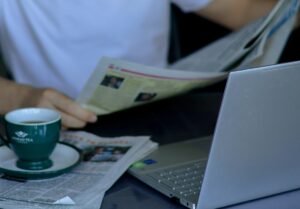 Homem lendo jornal ao lado do computador