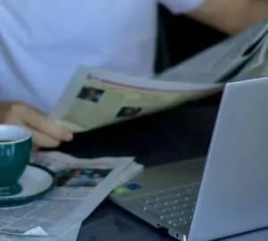 Homem lendo jornal ao lado do computador