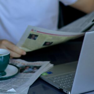 Homem lendo jornal ao lado do computador