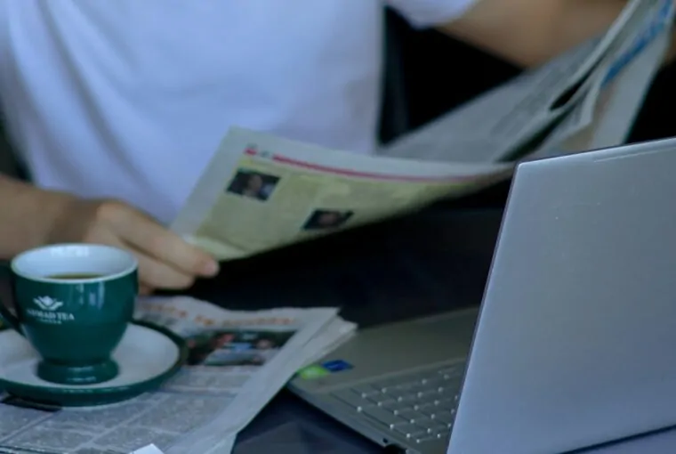 Homem lendo jornal ao lado do computador