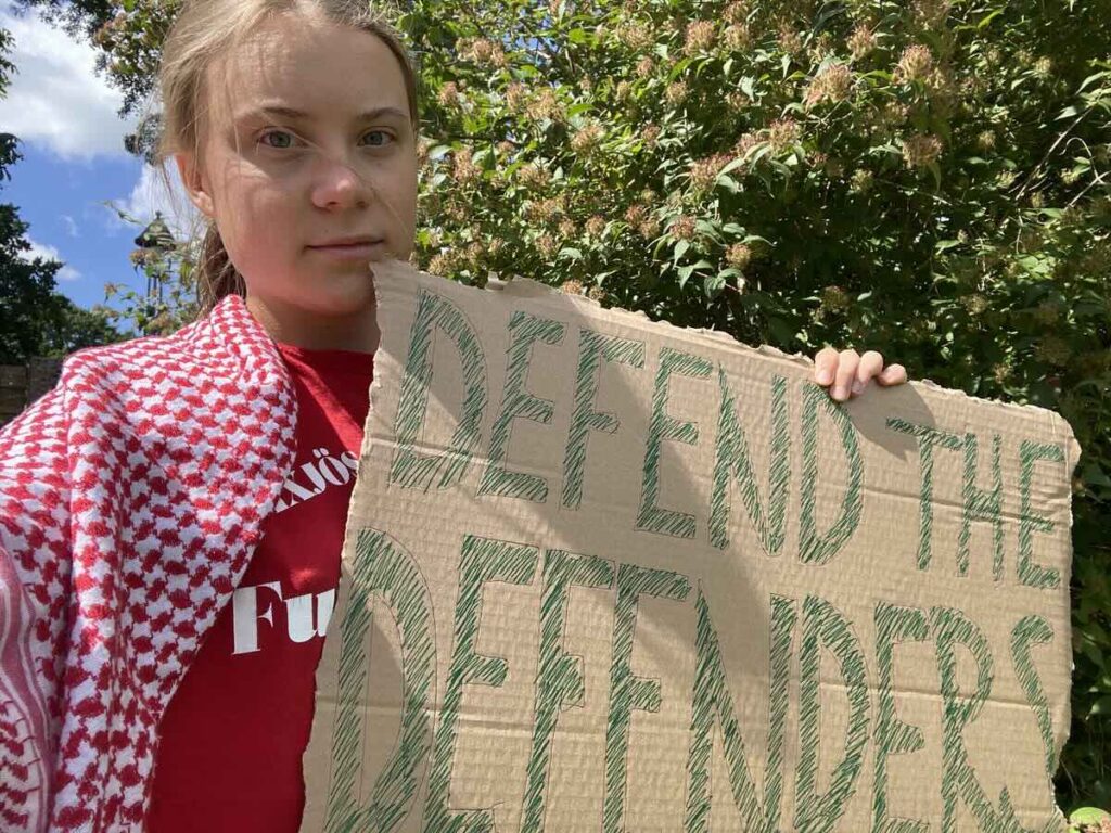 Greta Thumberg, ativista ambiental, segurando cartaz contra violência voltada a ativistas ambientais