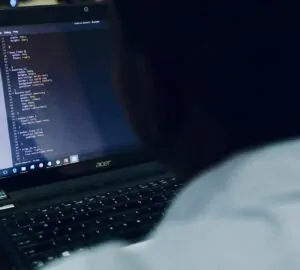 Homem no computador com tela exibindo códigos
