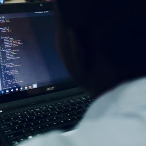 Homem no computador com tela exibindo códigos