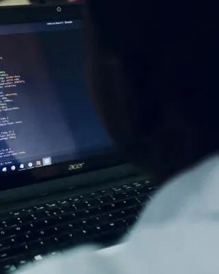 Homem no computador com tela exibindo códigos