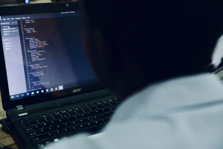 Homem no computador com tela exibindo códigos