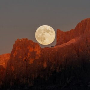 A Lua cheia surge sobre as montanhas Dolomitas, tingidas pelo dourado do pôr do sol.