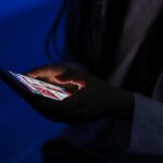 Adolescente olhando o celular no escuro, com a tela iluminando o rosto, em uma imagem que representa o impacto das fake news em jovens.