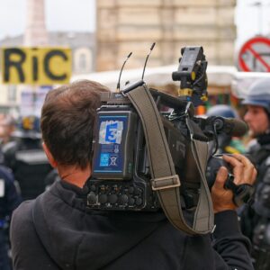 Cinegrafista em protesto com policiais ao fundo - cobertura livre de manifestações é uma das ameaças a jornalistas listadas pela ONU